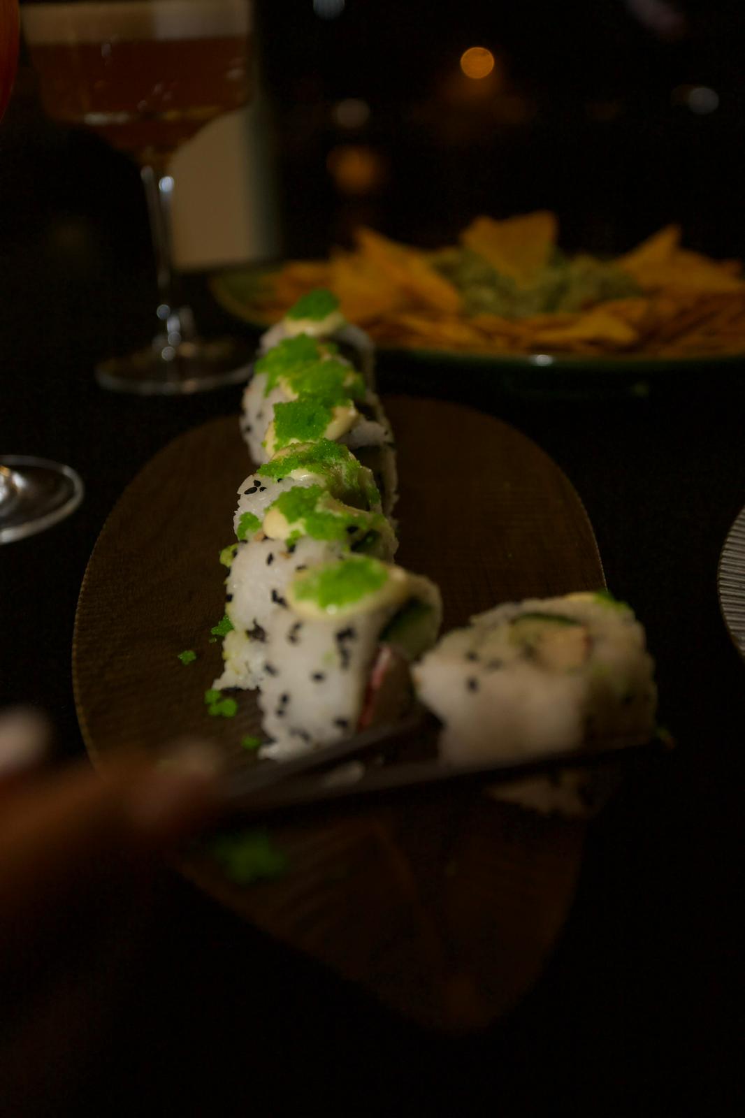 Sushi roll platter with cocktails and guacamole in the background